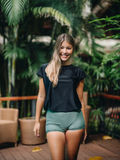 Woman in black swim top and green shorts standing in a tropical setting with plants.