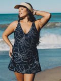 Woman standing on the beach wearing a black and white floral Alana Swim Dress | Plus Size, showcasing size-inclusive, modest swimwear with a comfortable fit and supportive design. Swimwear designed for every body.