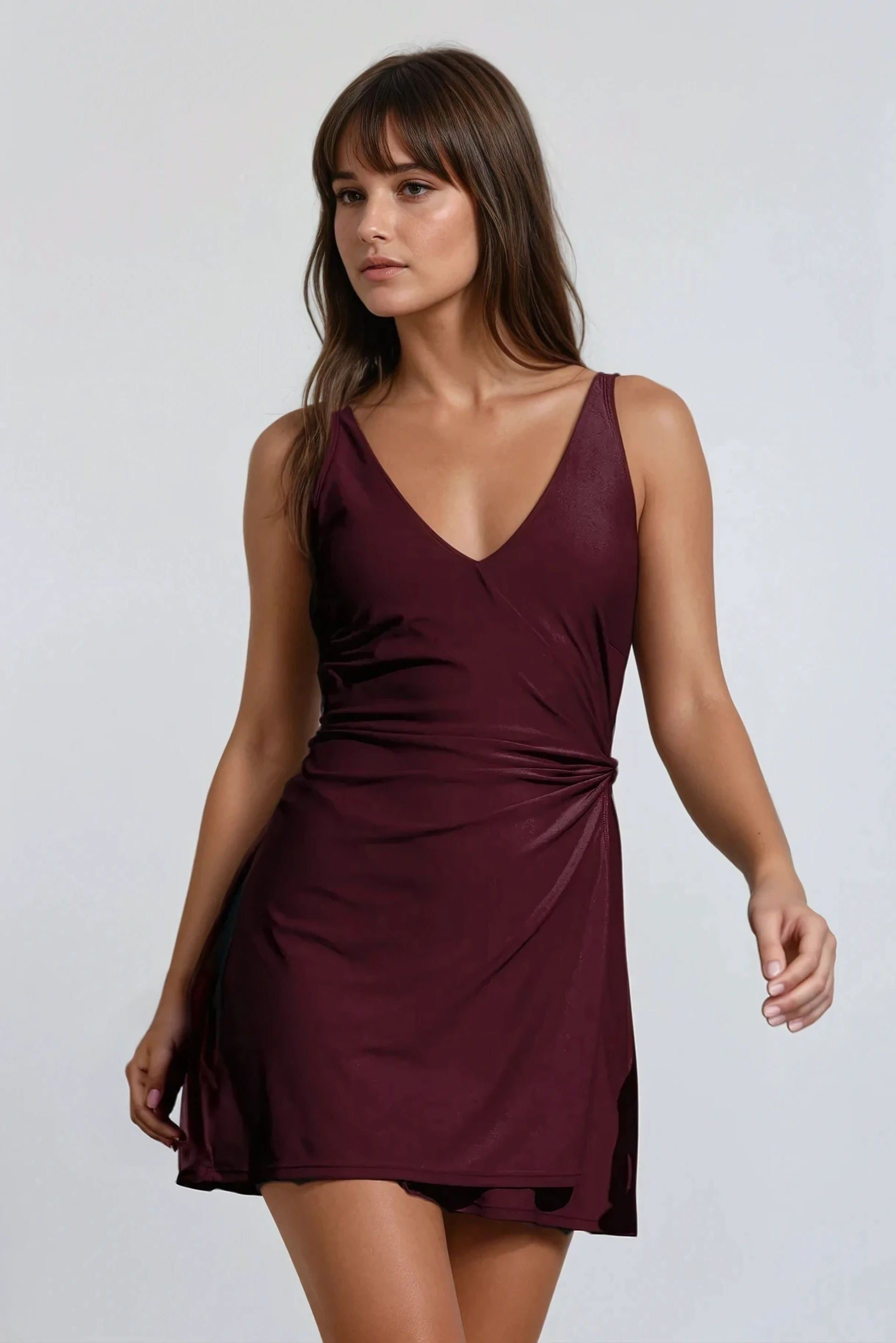 A woman wearing a green sleeveless swim dress with a v-neckline and decorative side tie, designed for plus-size with hidden bikini bottoms.