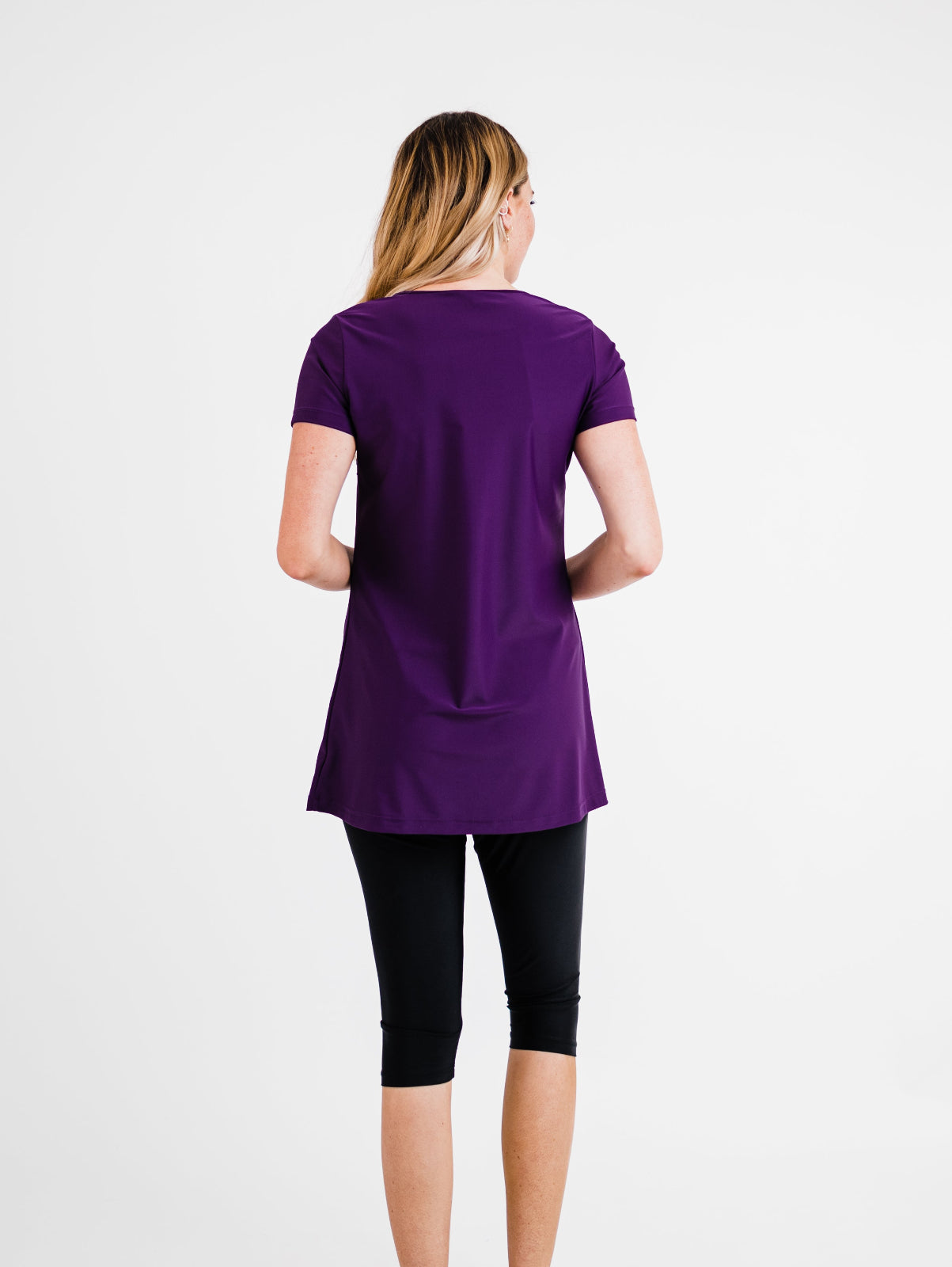 Person wearing a purple tunic and black leggings on a white background