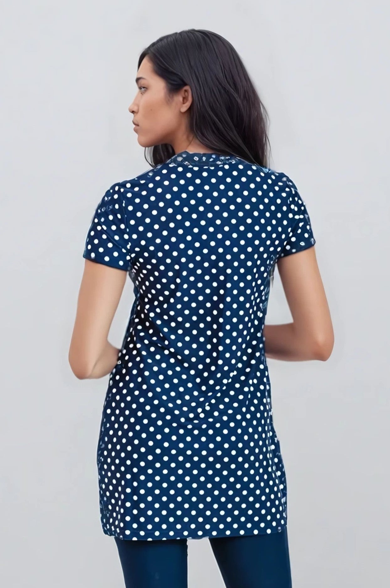 Woman wearing a navy blue tunic with white polka dots on a light gray background