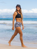 Boyshorts | Final sale model wearing patterned swim shorts and a black swim top while walking along the beach in comfortable size-inclusive swimwear for every body