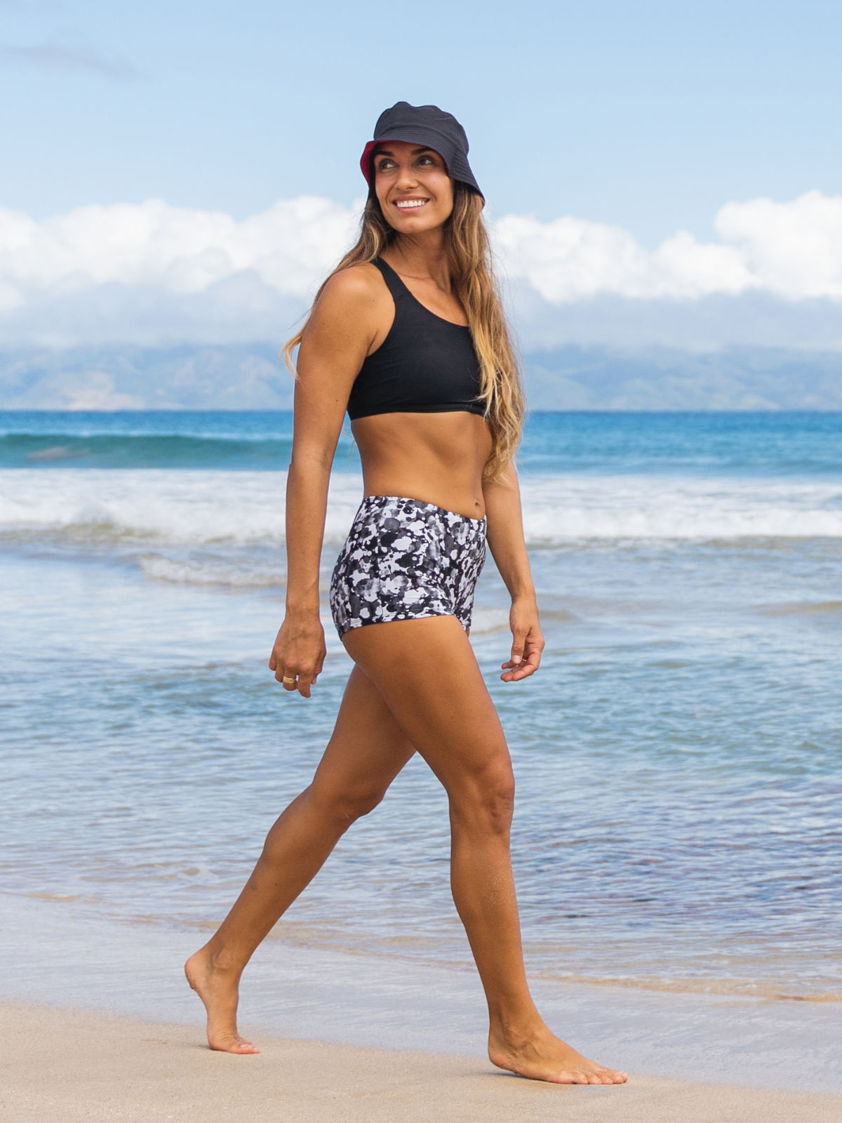 Boyshorts | Final sale model wearing patterned swim shorts and a black swim top while walking along the beach in comfortable size-inclusive swimwear for every body