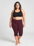 A confident plus size woman wearing burgundy Capri Swim Leggings | Plus Size paired with a black swim top, showcasing size-inclusive, modest, supportive swimwear with a comfortable fit. Swimwear designed for every body.
