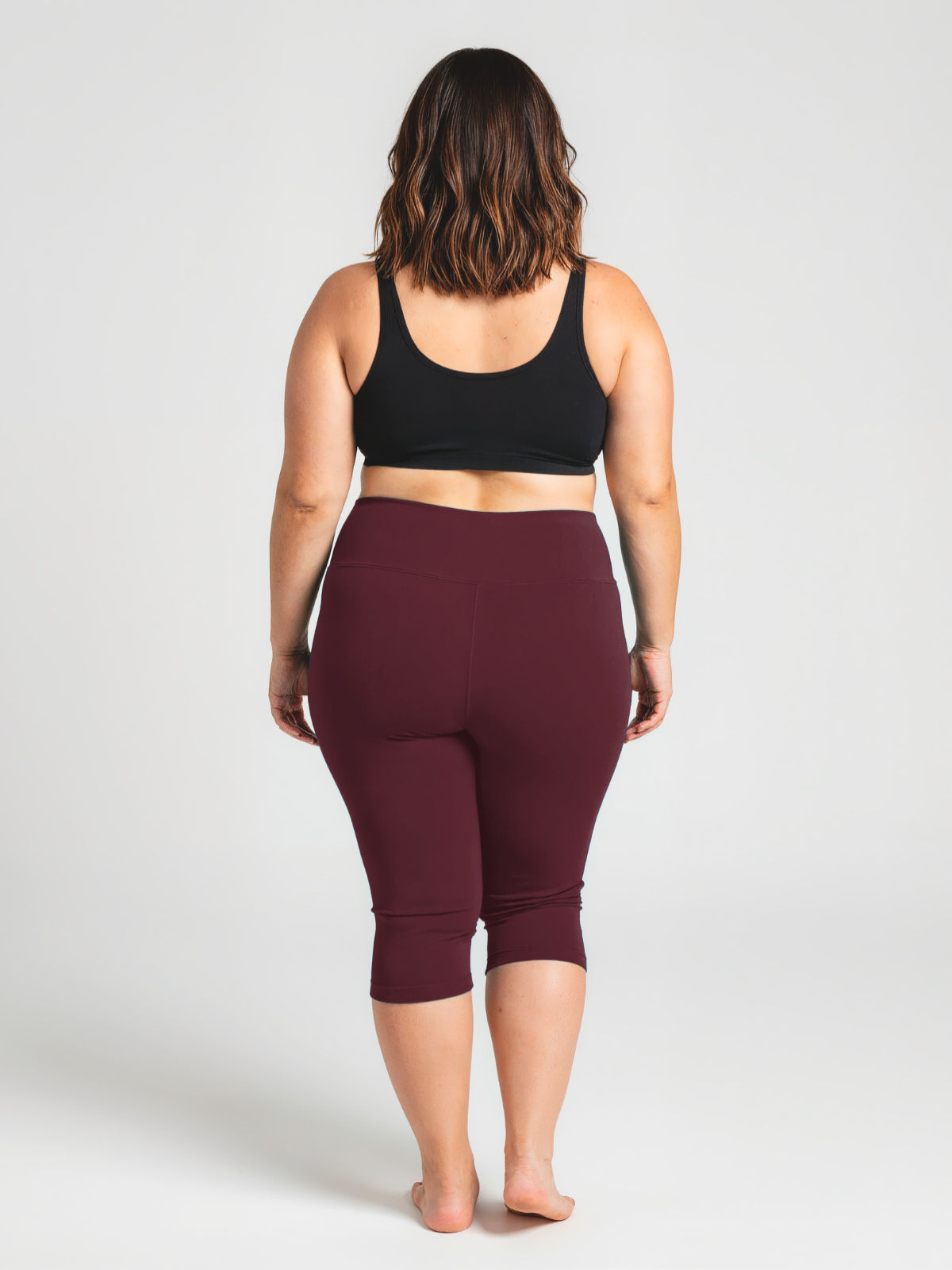 Woman shown from behind wearing deep wine-colored Capri Swim Leggings | Plus Size paired with a black supportive swim top, highlighting comfortable, size-inclusive, modest swimwear designed for every body.