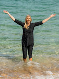 Woman wearing black Capri Swim Leggings and a matching swim top standing in shallow ocean water with arms raised