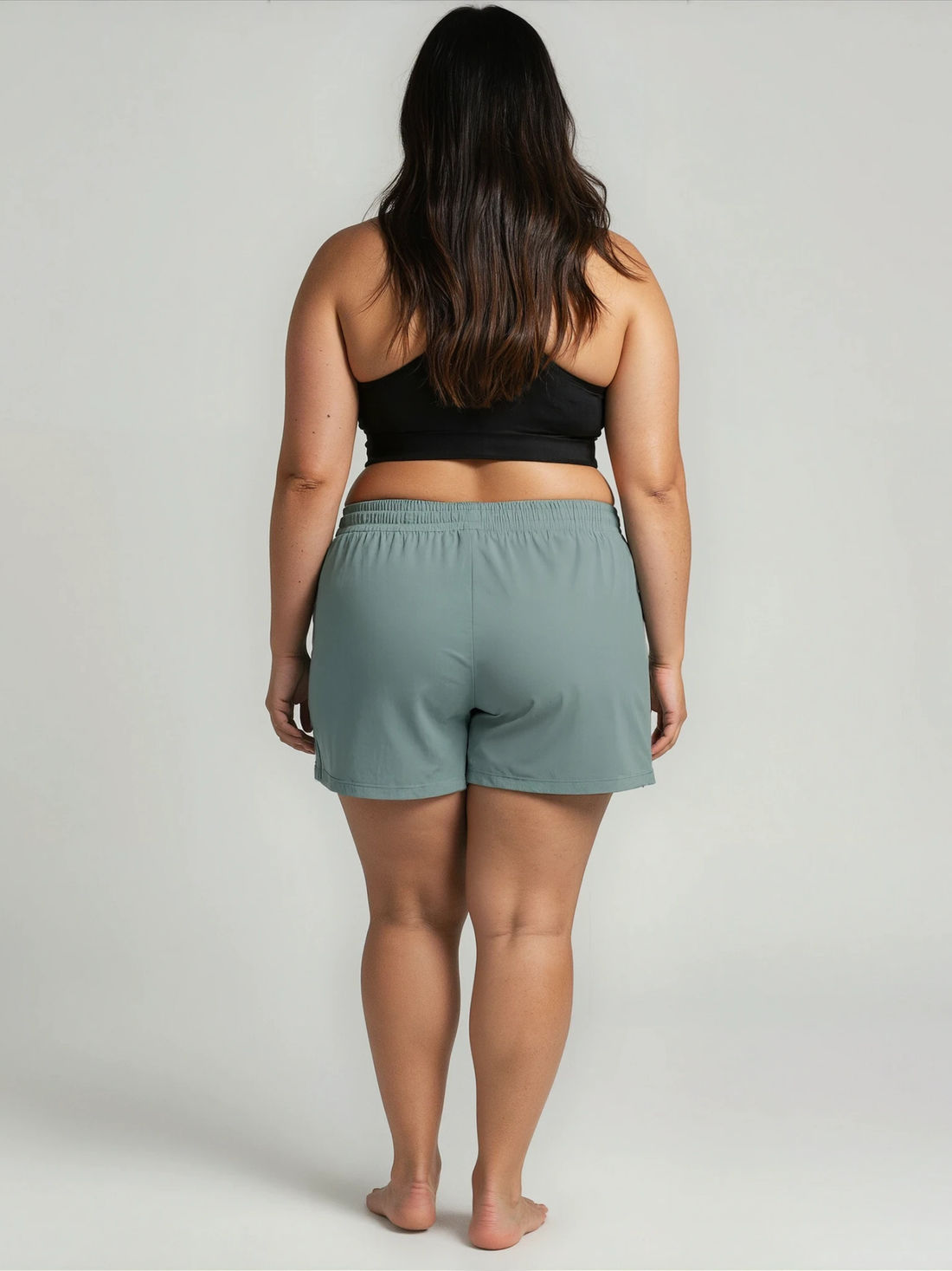 Woman wearing a black sports bra and light green shorts on a plain background