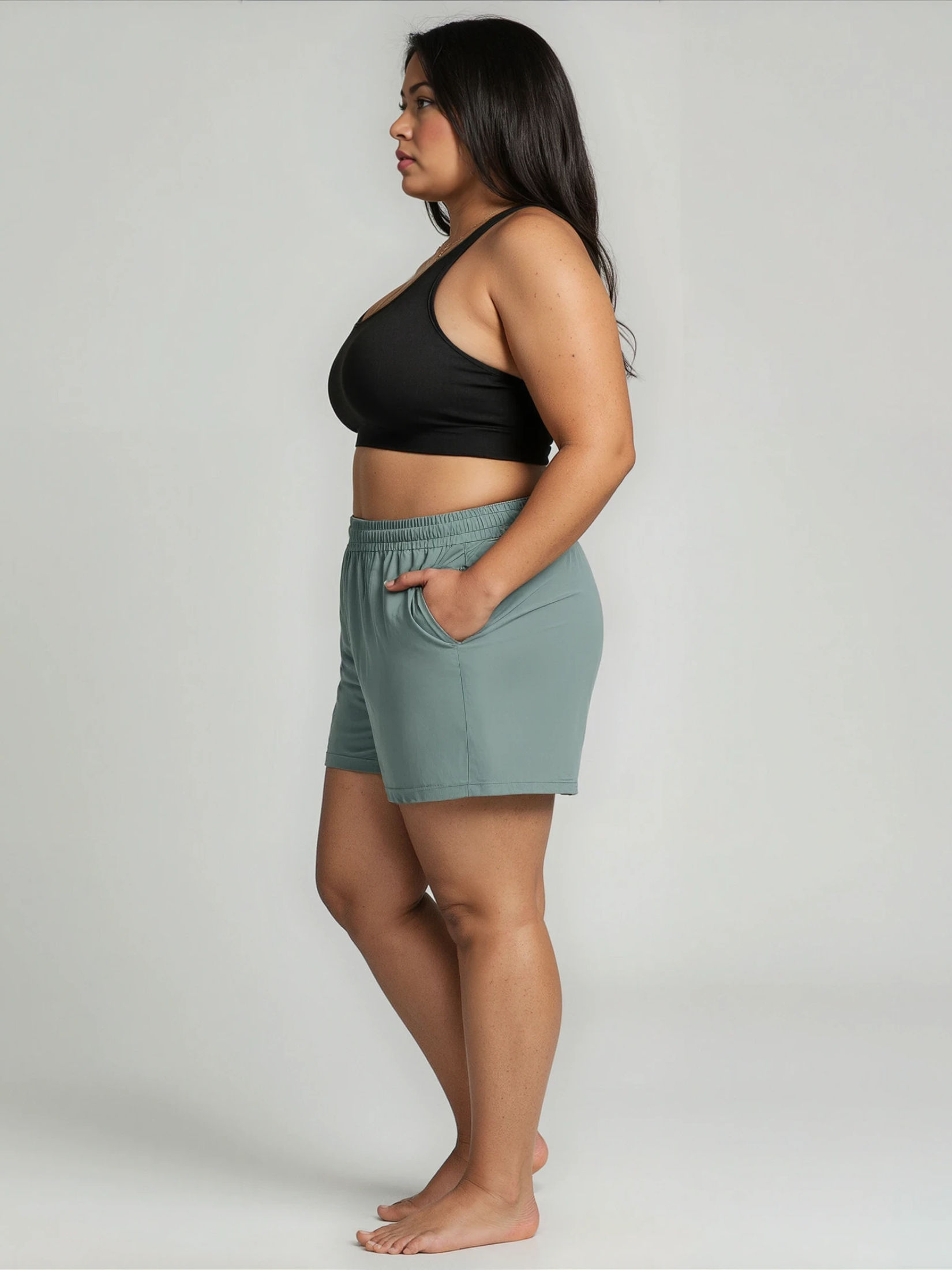Woman wearing a black sports bra and light green shorts on a plain background