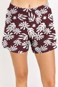 Maroon shorts with white floral pattern worn by a person on a plain background