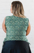 Person wearing a sleeveless top with a floral pattern against a white brick wall.