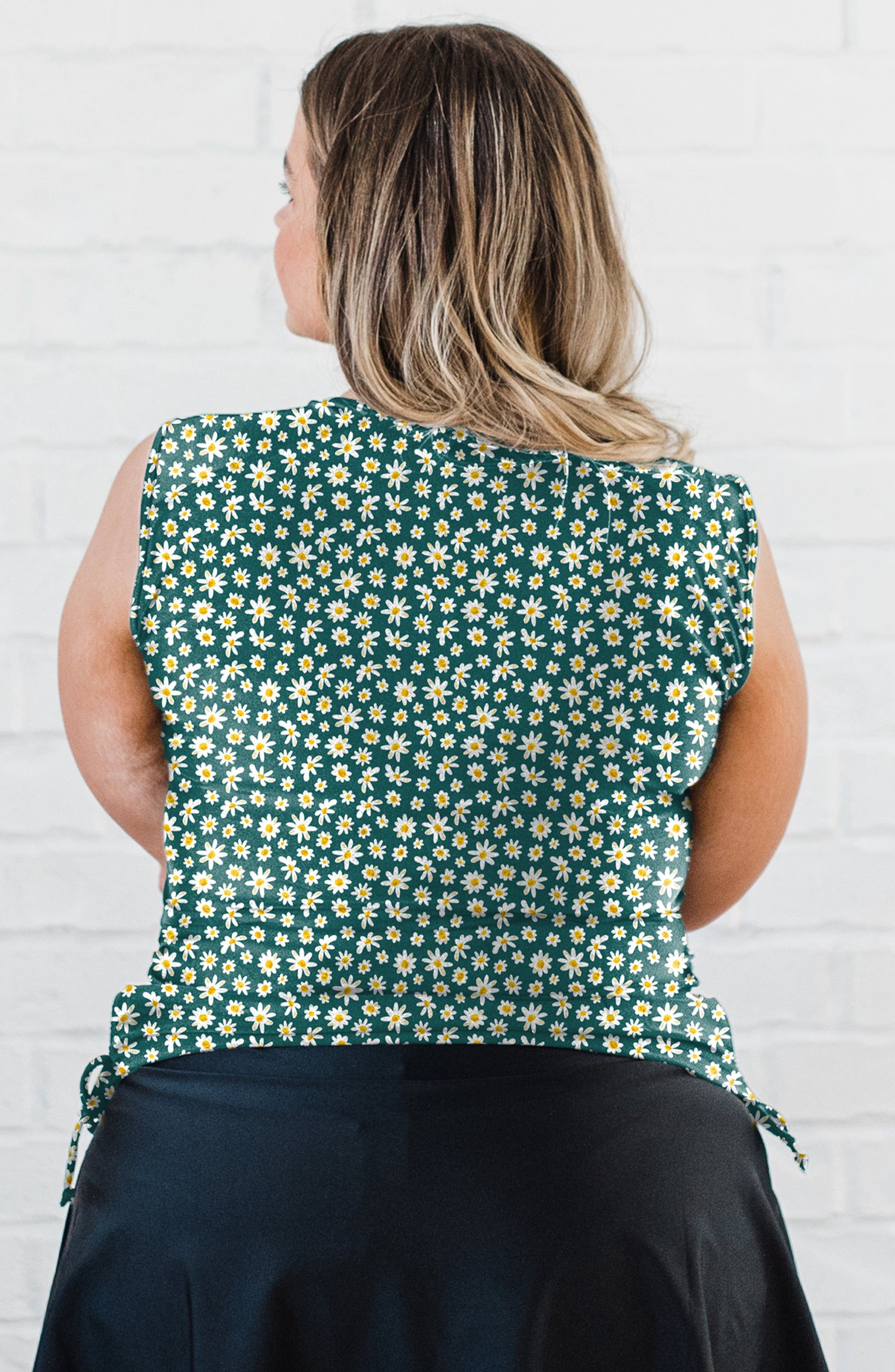 Person wearing a sleeveless top with a floral pattern against a white brick wall.