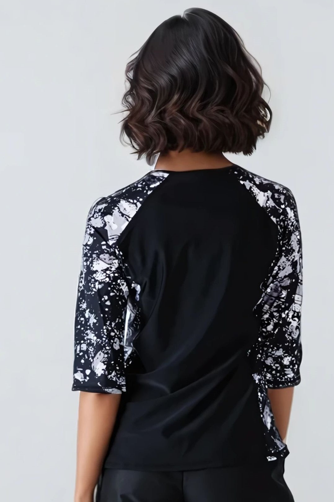 A model wearing a plus-size loose fit swim top with 3/4 length raglan sleeves and a round neckline. The top features green color with a floral pattern and contrasting side panels.