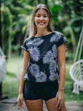 Woman wearing a black printed swim top with a white leaf pattern and black shorts outdoors.