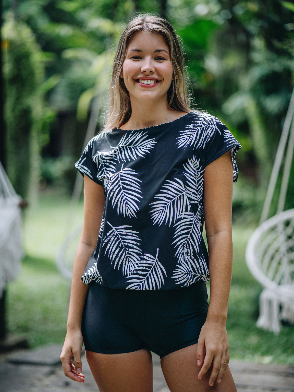 Woman wearing a black printed swim top with a white leaf pattern and black shorts outdoors.