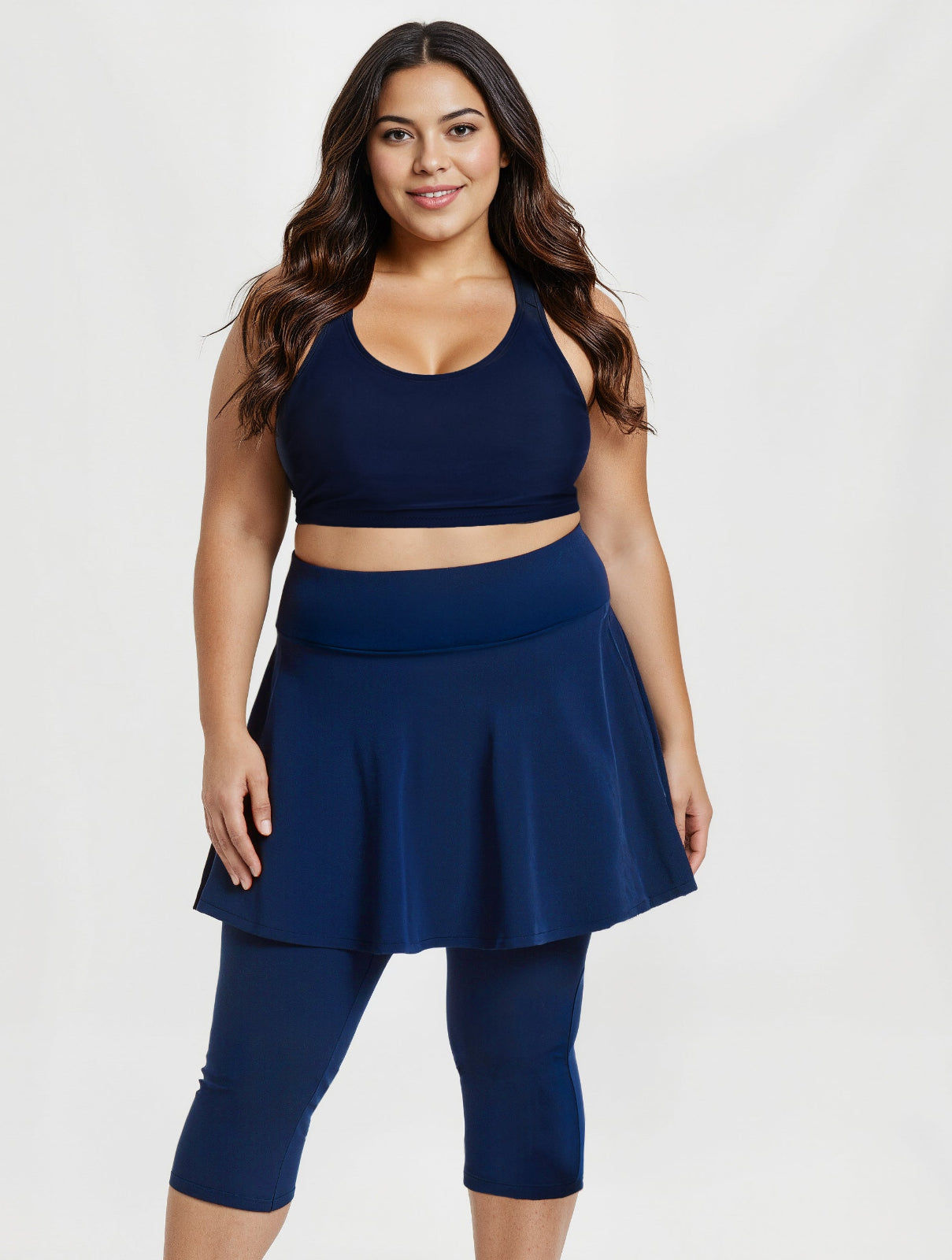 Model wearing Flared Swim Skort With Capri Leggings | Plus Size in navy with a fitted tank top and white sneakers showcasing supportive swimwear designed for every body.