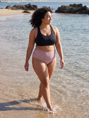 High Waisted Full Coverage Bikini Bottom | Plus Size worn by a woman walking through shallow beach water in supportive size-inclusive swimwear designed for every body