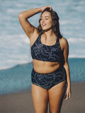 Woman smiling on the beach wearing a High Waisted Full Coverage Bikini Bottom | Plus Size in a dark floral pattern, showcasing size-inclusive, modest, supportive swimwear designed for every body.