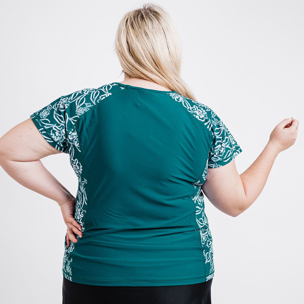 Back view of a plus size woman wearing a dark jade Loose Fit Adele Swim Top | Final Sale with white floral side panels, showcasing size-inclusive, comfortable, and supportive swimwear designed for every body.