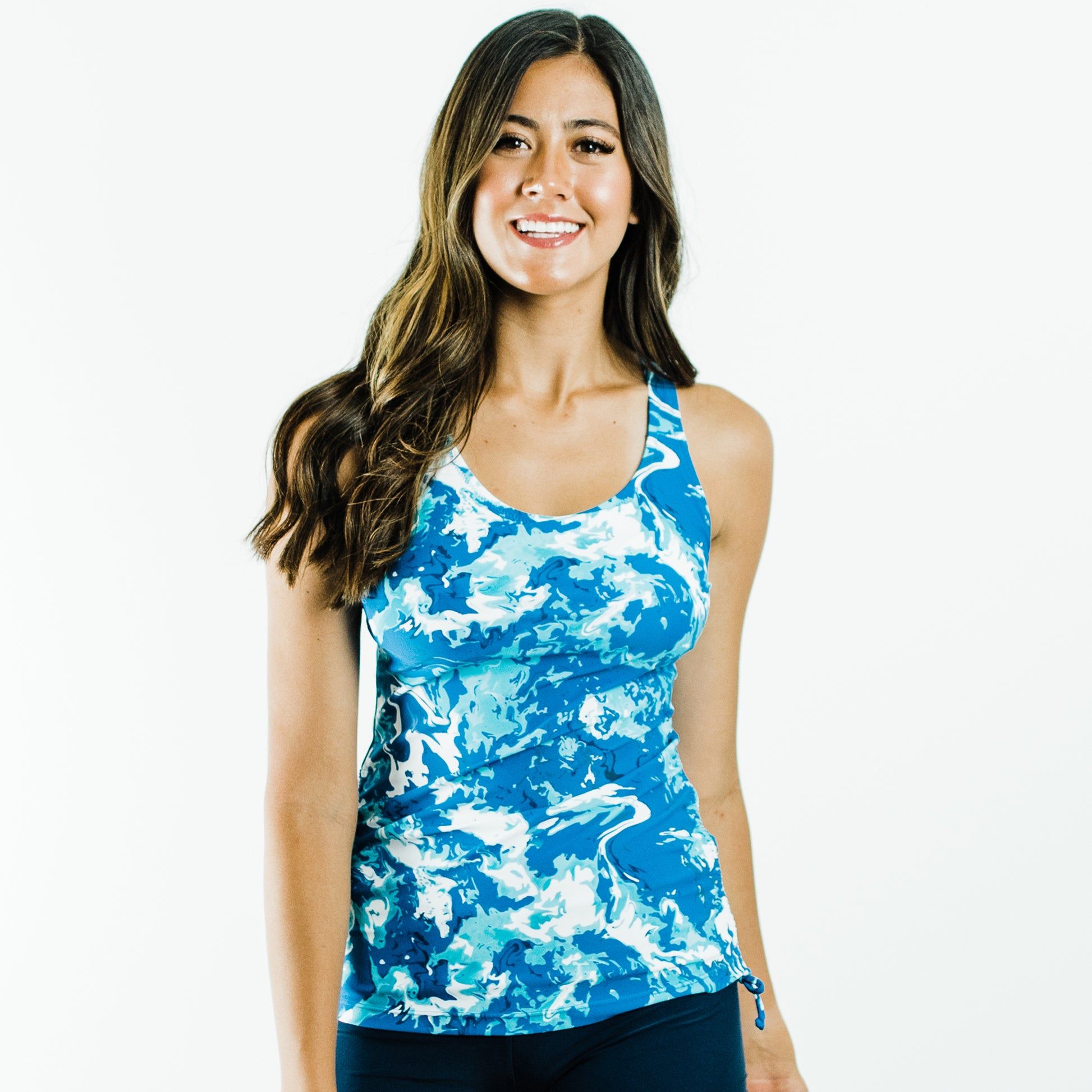 Woman wearing a blue patterned swim top smiling confidently showcasing the Maya Tankini Swim Top With Removable Cups | Final Sale, designed for a comfortable and supportive fit.