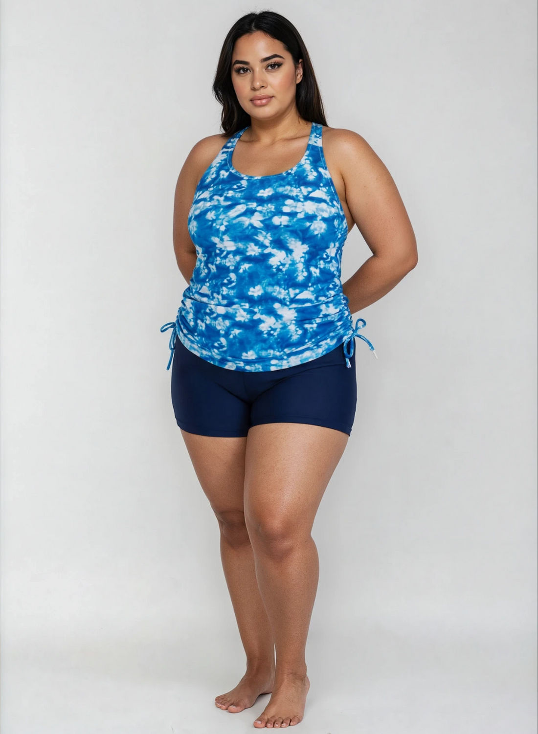 A woman modeling a blue and white tie-dye halter tank top with matching navy blue swim shorts against a light gray studio background.