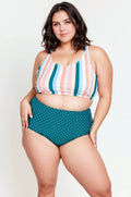 Woman wearing a colorful striped top and teal polka dot high-waisted shorts on a white background