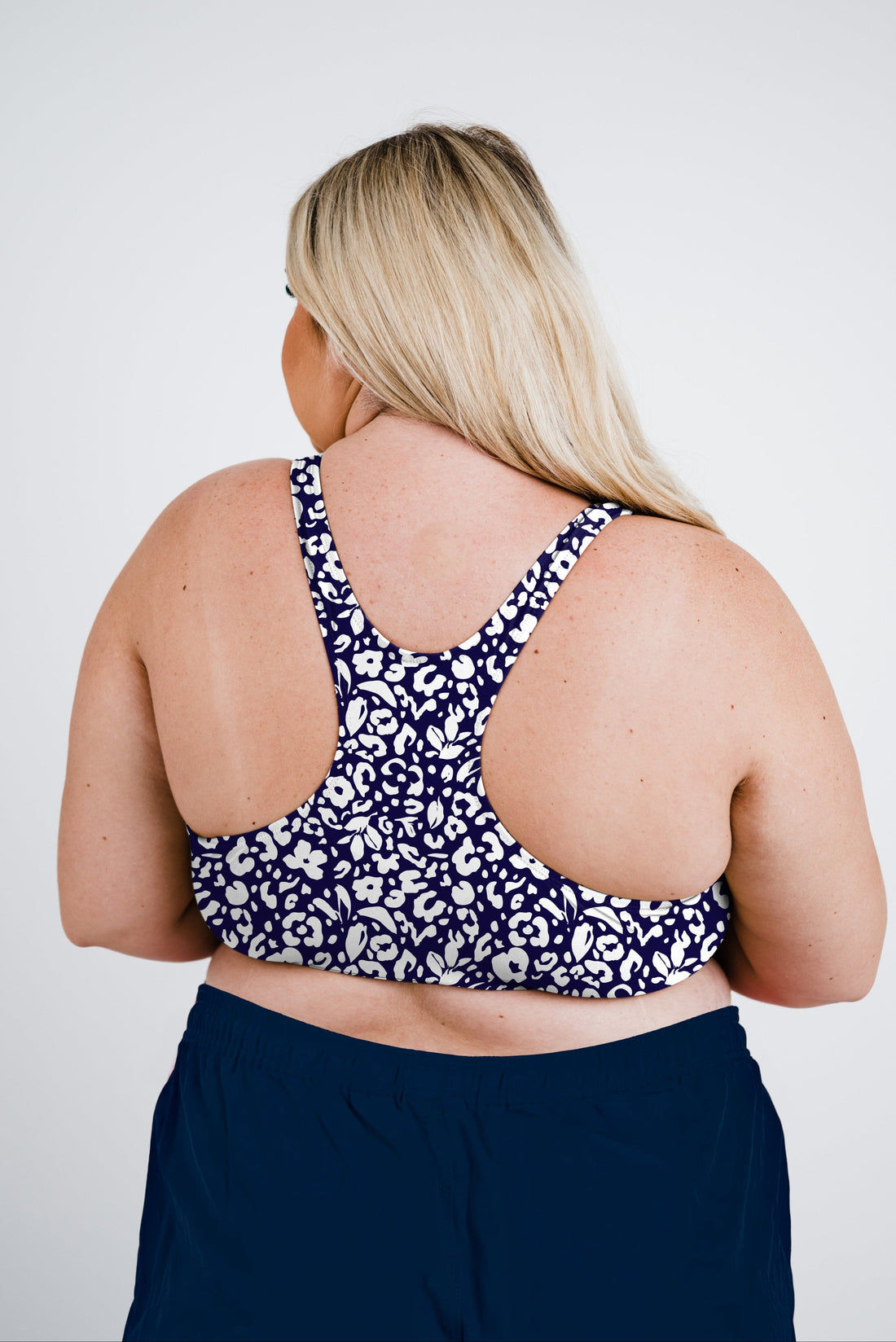 Woman wearing a patterned Racerback Swim Bra | Plus Size standing on the beach with arms raised, showcasing size-inclusive, supportive swimwear designed for every body.