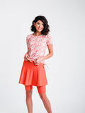 Woman wearing a floral top and orange skirt on a white background