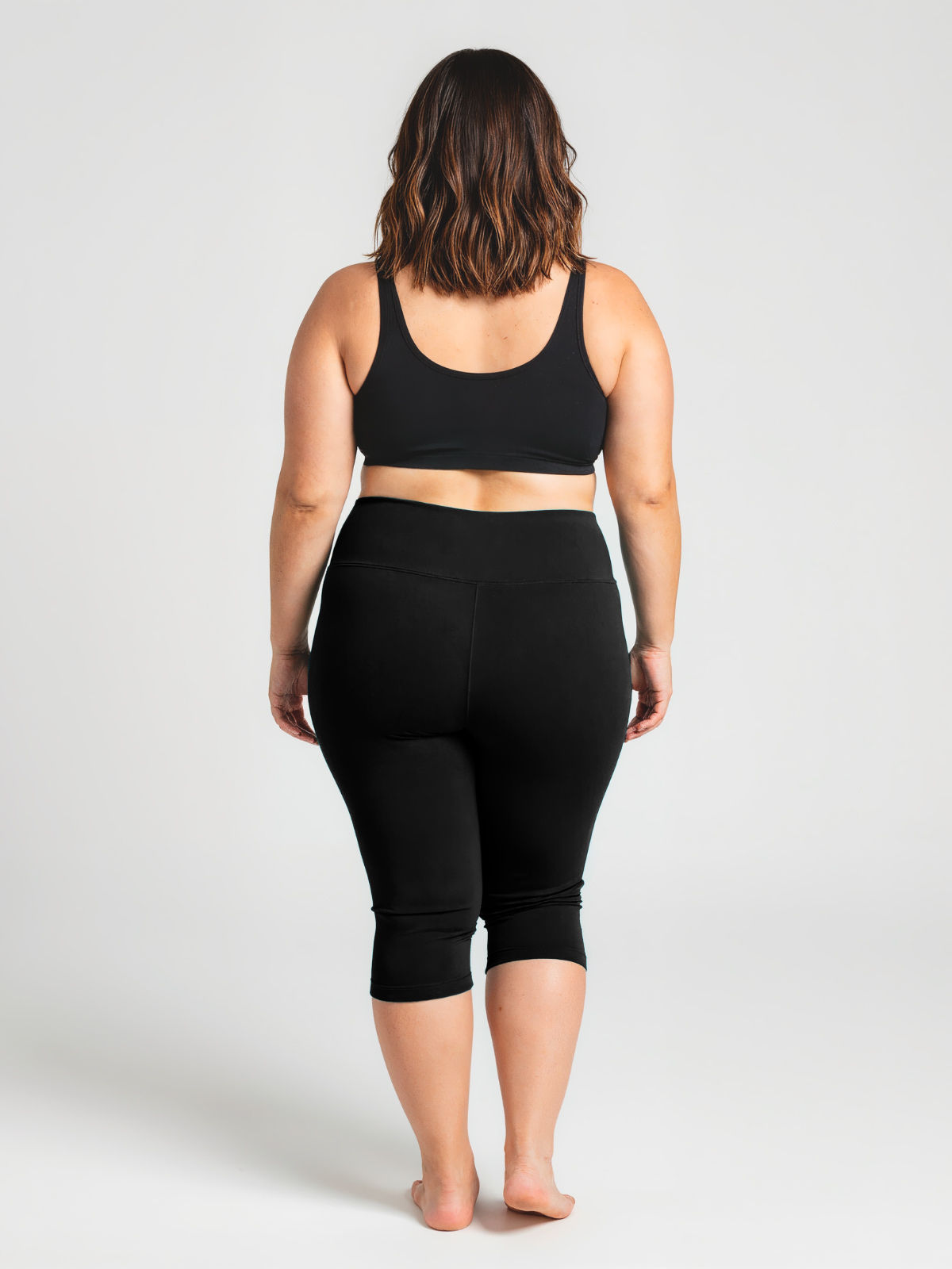Woman seen from behind wearing black Capri Swim Leggings | Plus Size paired with a supportive black swim top, showcasing size-inclusive, modest swimwear designed for a comfortable fit. Swimwear designed for every body.
