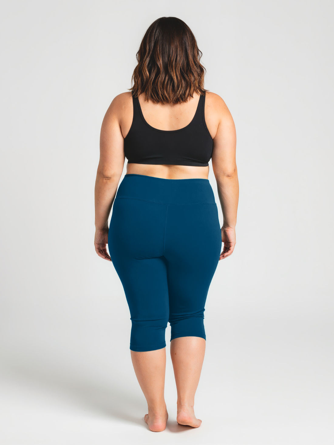 A confident plus size woman wearing Capri Swim Leggings | Plus Size in a deep blue color paired with a black supportive swim top, showcasing size-inclusive, modest swimwear designed for every body.
