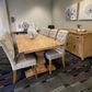 A wooden dining table with six tufted upholstered chairs in a staged dining room setting, featuring a matching wooden sideboard and patterned carpet.