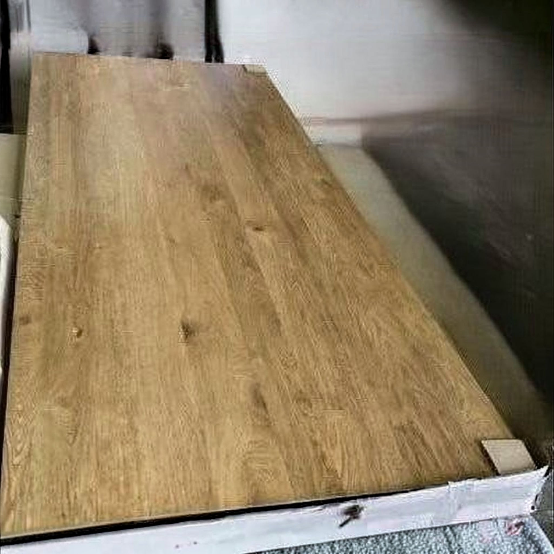 A large rectangular wood-look panel or tabletop with a light to medium brown grain pattern, resting on a white support frame in an indoor setting.