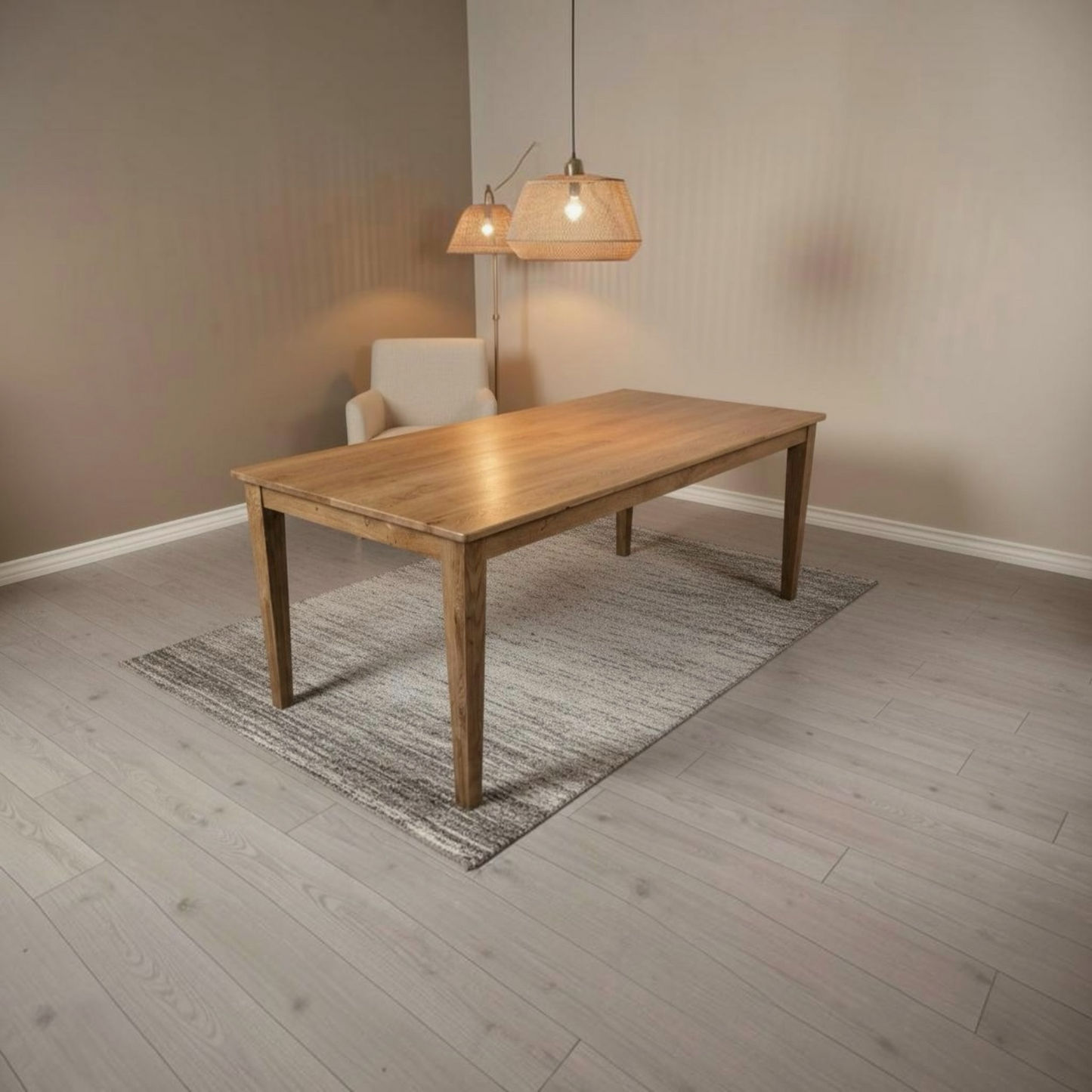 A rectangular wooden dining table with a natural oak finish, styled on a gray patterned rug in a modern dining room setting with a white armchair and two hanging pendant lights.