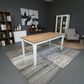 A rectangular dining table with a light natural wood top and white legs, shown in a styled dining room setting on a gray and white patterned rug.
