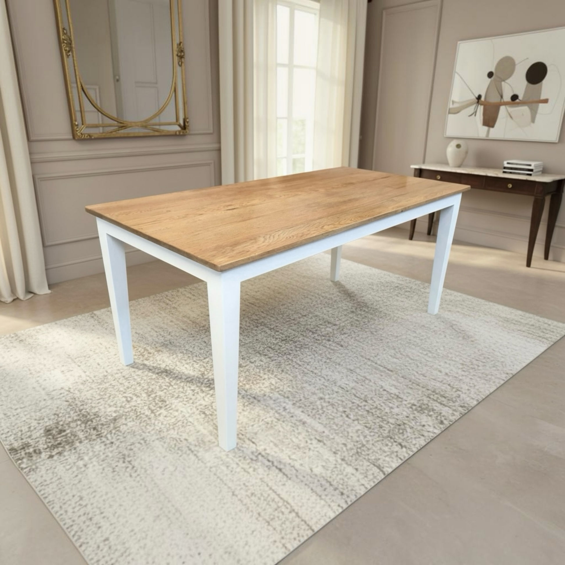 A rectangular dining table with a light oak wood top and white legs, placed on a textured cream rug in a bright, modern dining room.
