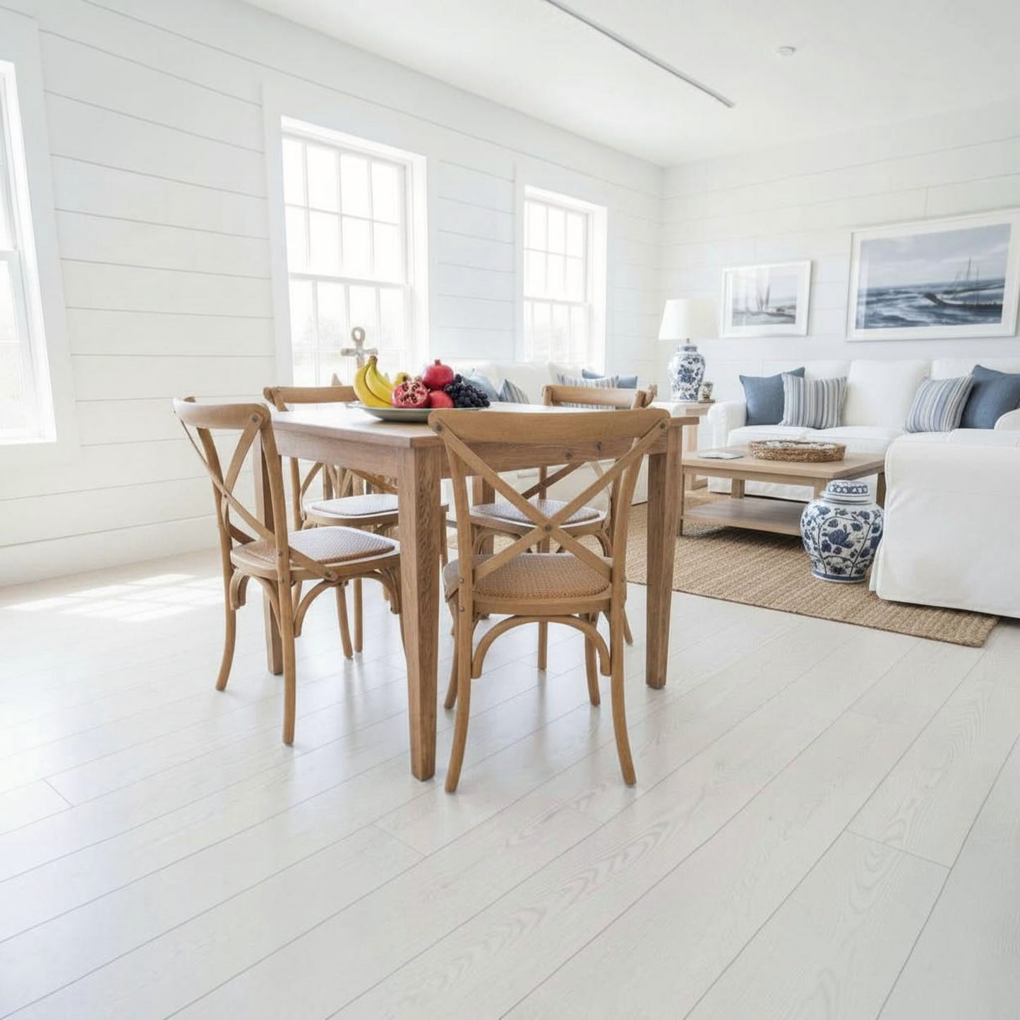 A light natural wood dining table with four matching wooden chairs in a bright, modern dining room with white shiplap walls and light wood floors.