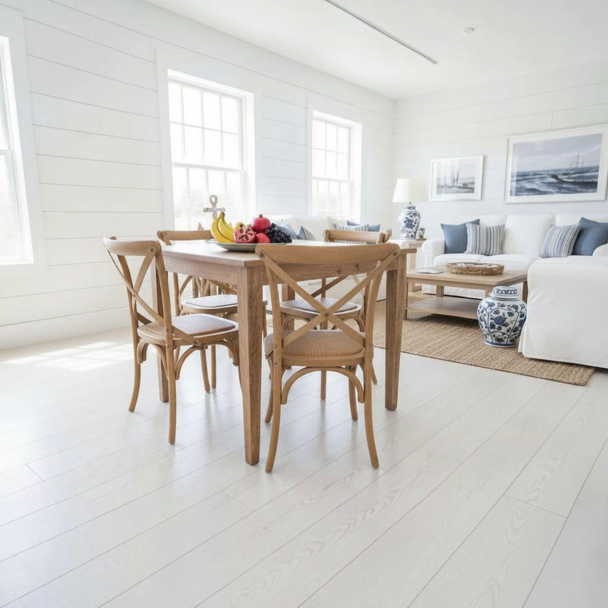 A light natural wood dining table with four matching wooden chairs in a bright, modern dining room with white shiplap walls and light wood floors.
