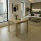 A light natural wood dining table with rustic weathered edges and four legs, styled with a small green glass vase and a white bowl in a bright, modern living room with beige floors and a white sectional sofa.