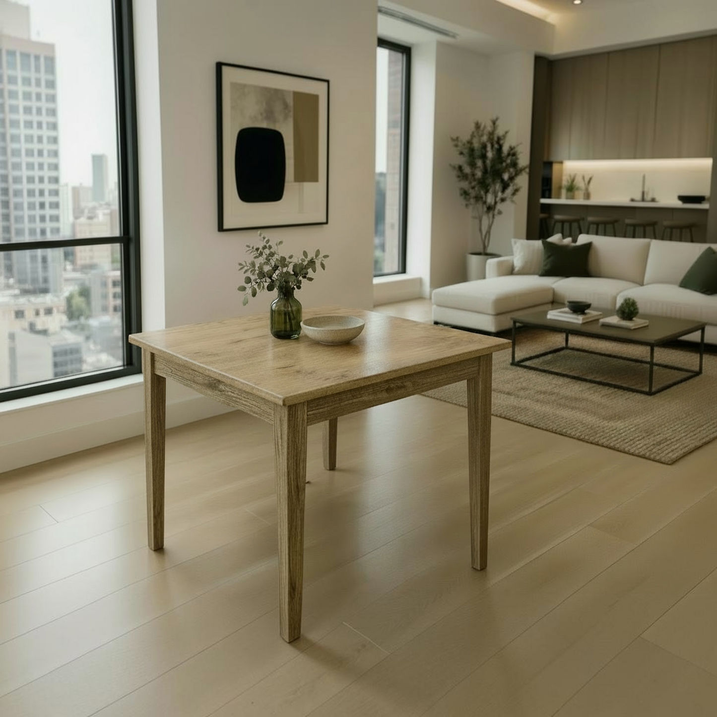 A light natural wood dining table with rustic weathered edges and four legs, styled with a small green glass vase and a white bowl in a bright, modern living room with beige floors and a white sectional sofa.