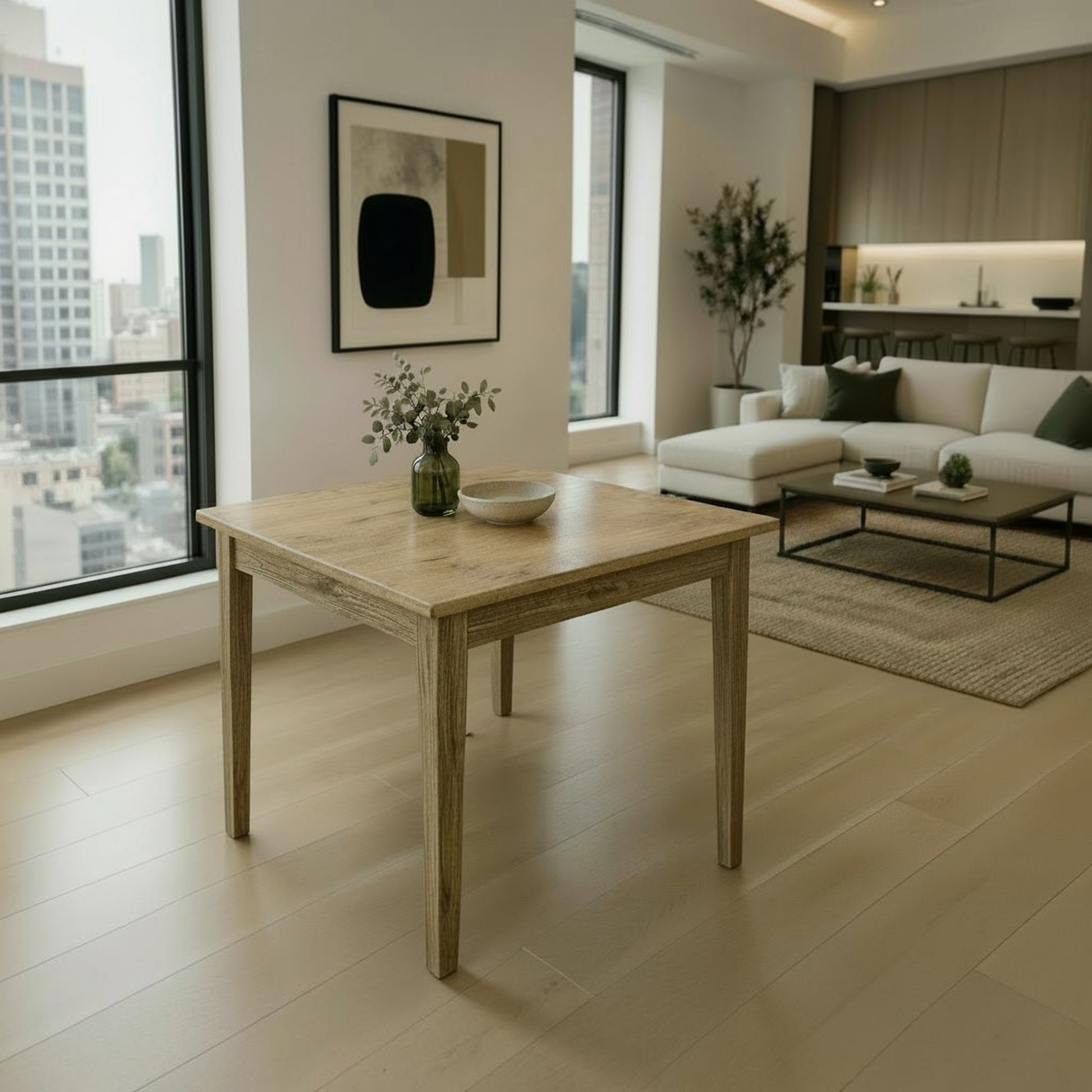 A light natural wood dining table with rustic weathered edges and four legs, styled with a small green glass vase and a white bowl in a bright, modern living room with beige floors and a white sectional sofa.
