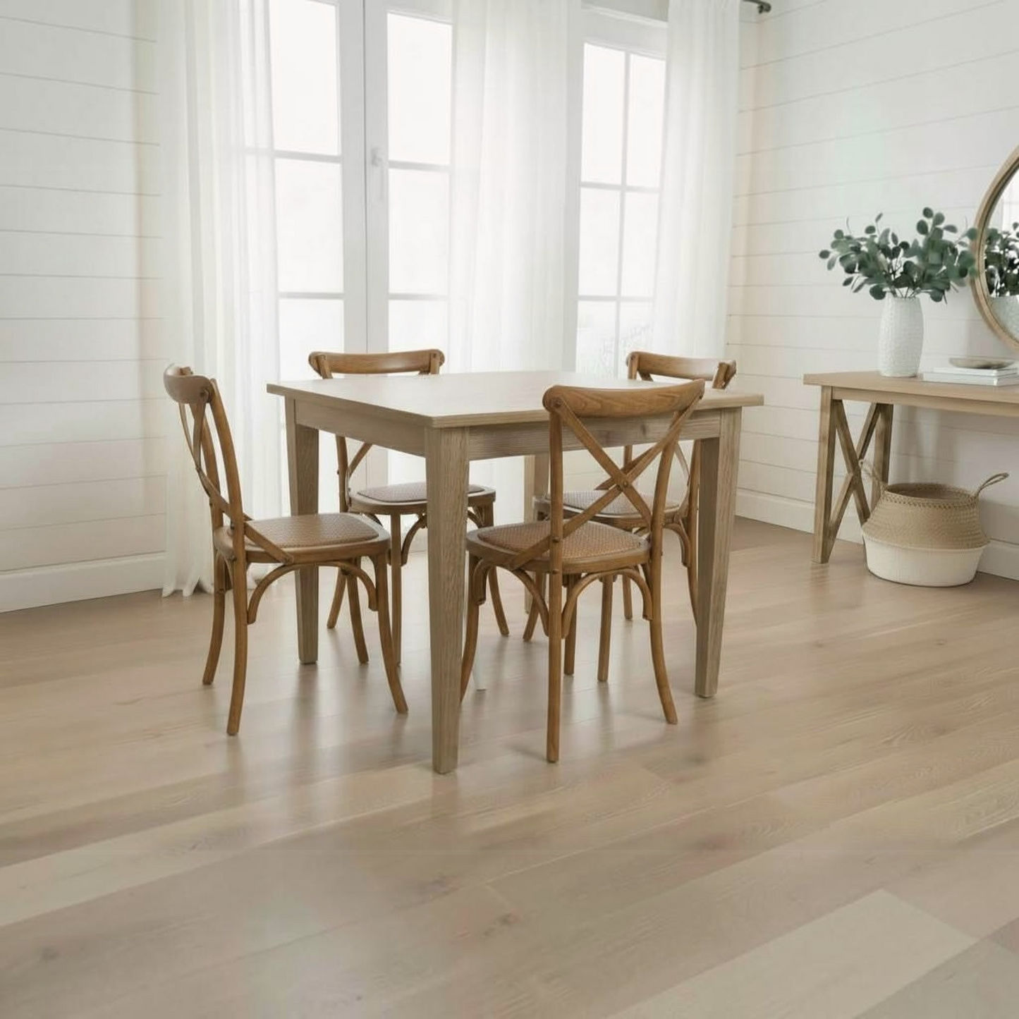 A light oak dining table with four matching wooden chairs in a bright, modern dining room with white shiplap walls and light wood floors.
