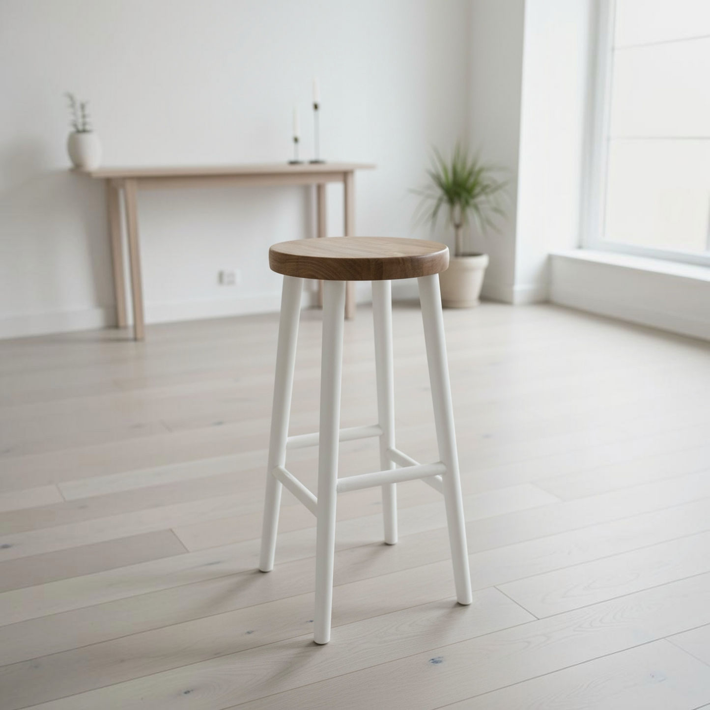 A modern bar stool with a round natural wood seat and four painted white legs, positioned in a bright, minimalist room with light wood floors and a console table in the background.