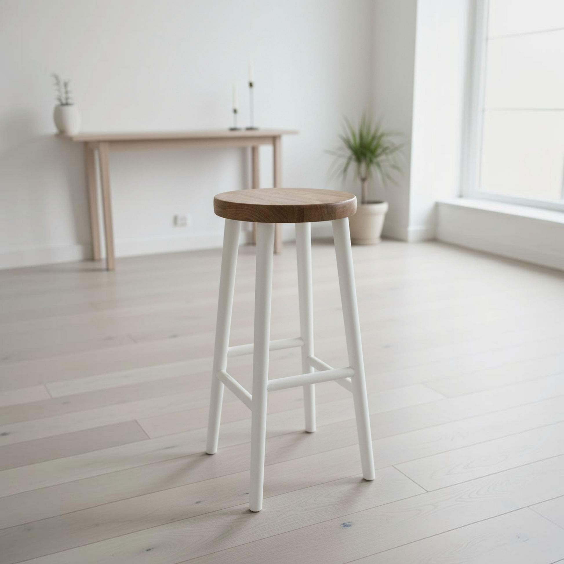 A modern bar stool with a round natural wood seat and four painted white legs, positioned in a bright, minimalist room with light wood floors and a console table in the background.