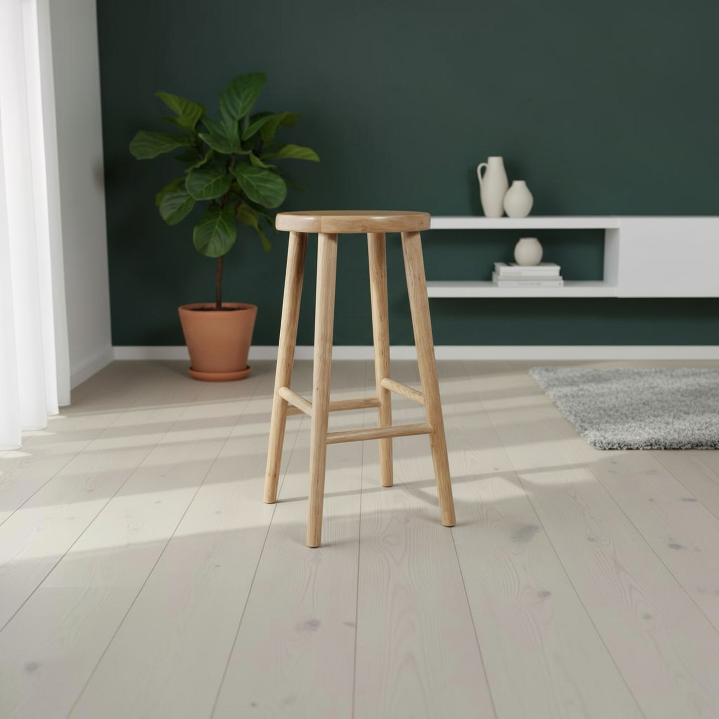 A light natural wood bar stool with a round seat and four legs, shown in a modern room setting with a dark green wall, white floating shelf, and a potted plant.