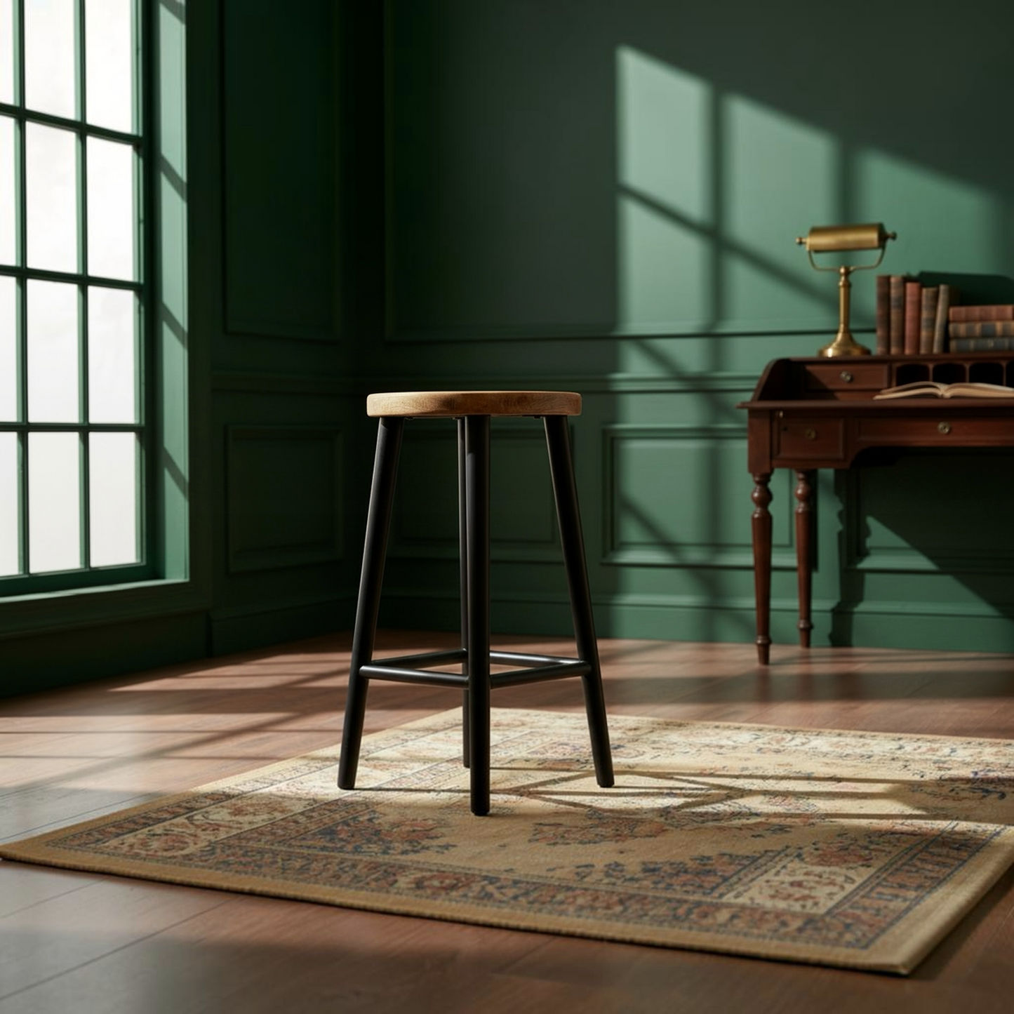 A wooden bar stool with a light oak seat and black legs stands on a vintage-style patterned rug in a sunlit room with dark green paneled walls and a desk.