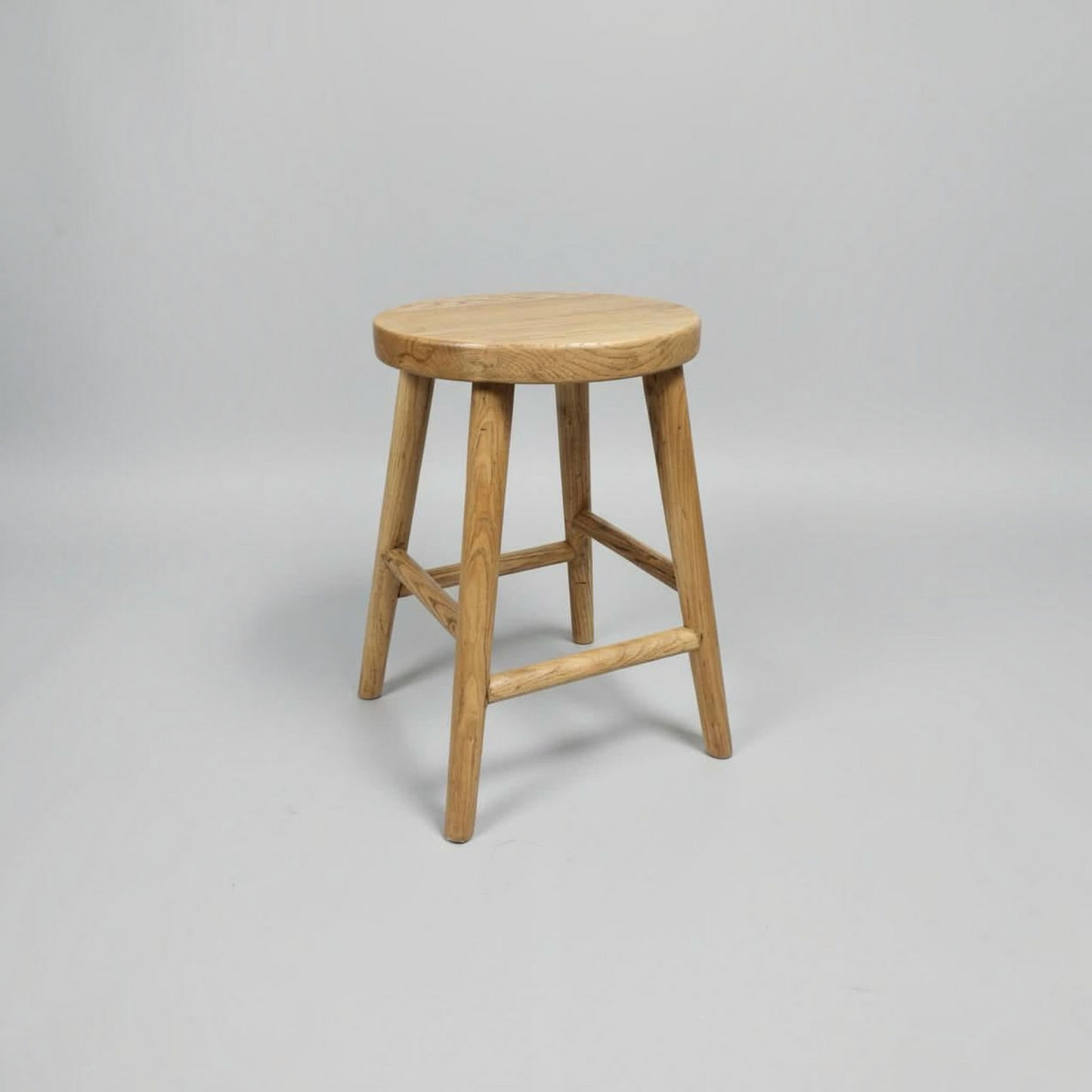 A light natural wood stool with a round seat and four angled legs, shown on a neutral light gray background.