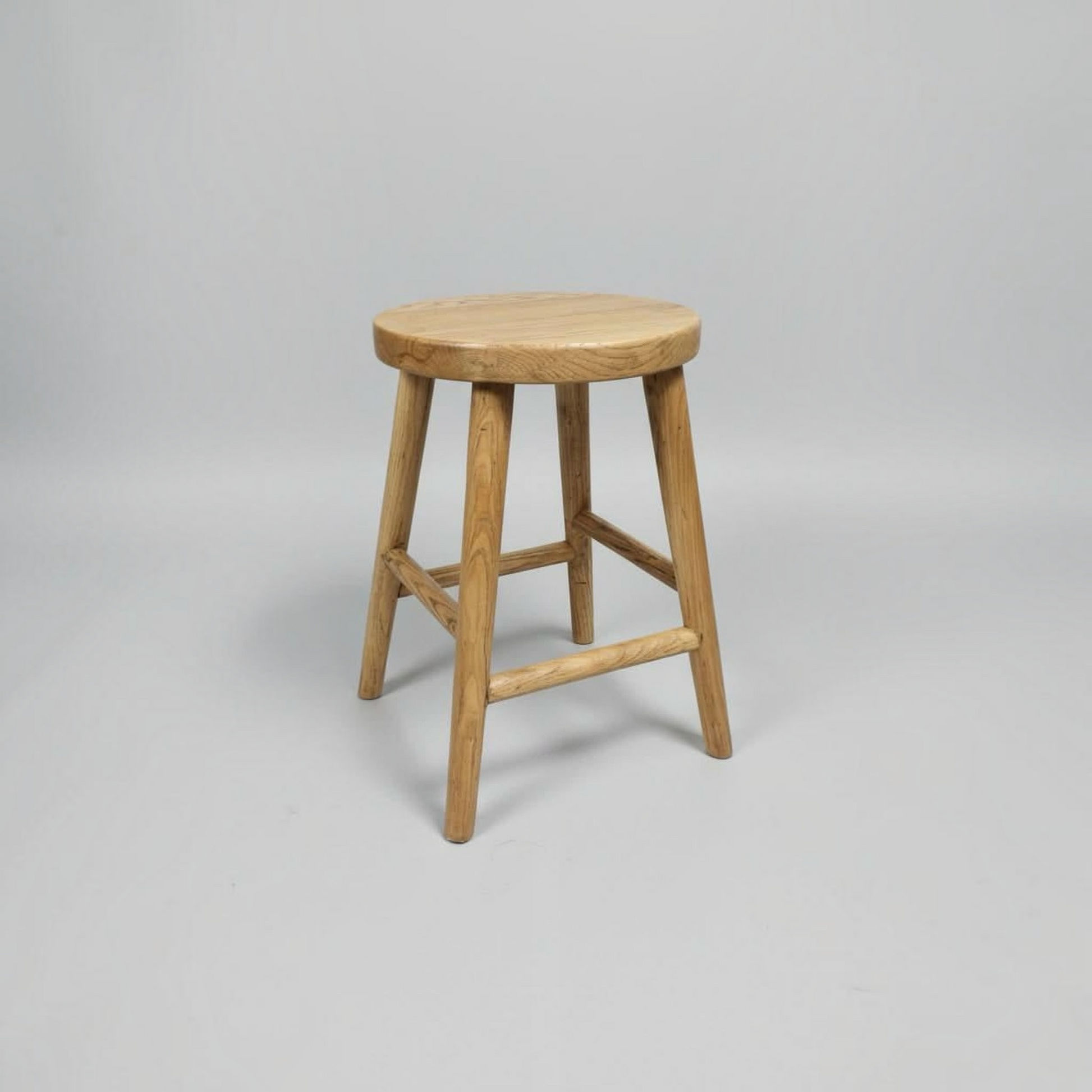 A light natural wood stool with a round seat and four angled legs, shown on a neutral light gray background.