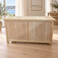 A light natural wood chest or trunk with two front doors, shown in a bright room with wood flooring and a large window overlooking water.