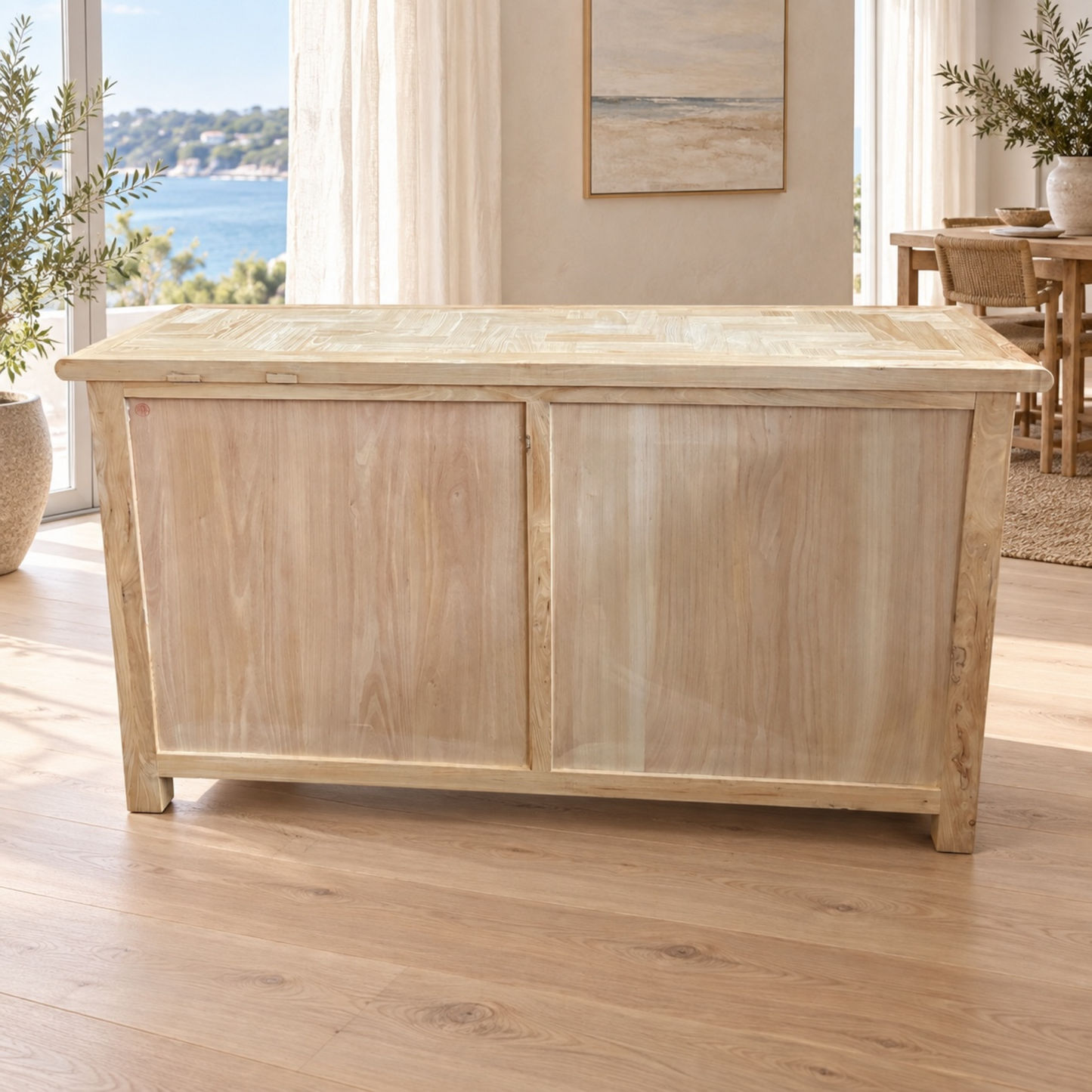 A light natural wood chest or trunk with two front doors, shown in a bright room with wood flooring and a large window overlooking water.
