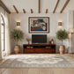 A styled living room interior featuring a dark wood media console with a television, a large framed abstract painting on the textured wall, two potted olive trees, a patterned area rug, and warm ambient lighting.