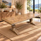 A rustic rectangular wooden dining table with a geometric inlay pattern on the top and turned pedestal legs, styled in a bright coastal-themed dining room on a woven rug.